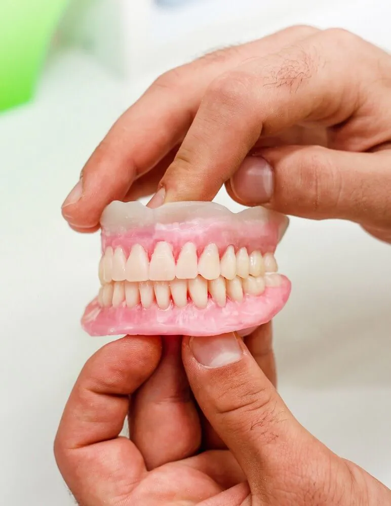 Mãos segurando uma prótese protocolo dentária (reabilitação oral fixa sobre implantes) na clínica Ferdinand Odontologia, na Tijuca, Rio de Janeiro