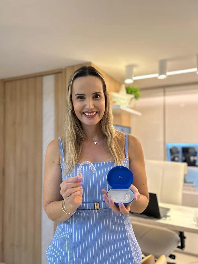Dentista na Spazio Vita em Linhares ES sorrindo ao segurar alinhador invisível Invisalign e sua caixinha azul no consultório.