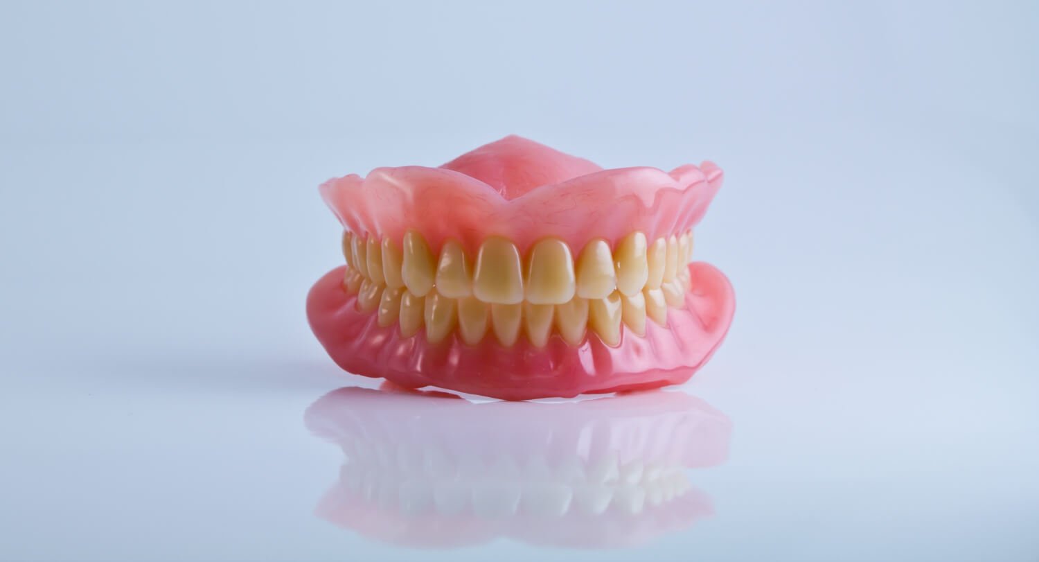 Dentadura completa superior e inferior sobre superfície reflexiva branca, ilustrando o problema de dentadura frouxa em Linhares ES.